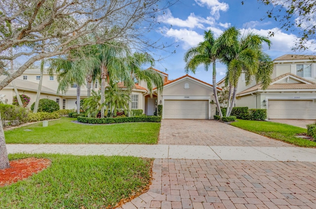 view of front of house featuring decorative driveway, a tile roof, stucco siding, an attached garage, and a front yard