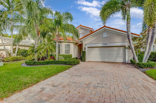 mediterranean / spanish home featuring decorative driveway, a tile roof, stucco siding, a garage, and a front lawn