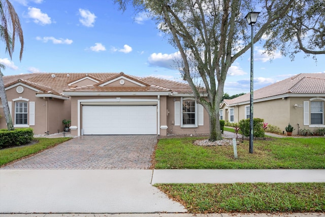 ranch-style home with decorative driveway, stucco siding, a garage, a tiled roof, and a front lawn