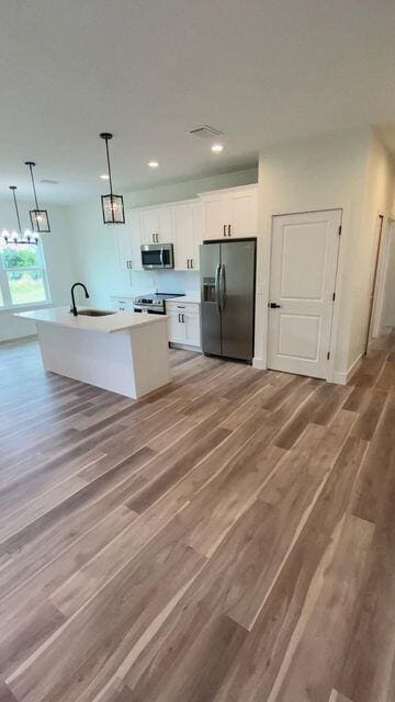 kitchen with fridge with ice dispenser, a sink, stainless steel microwave, white cabinetry, and light wood-style floors