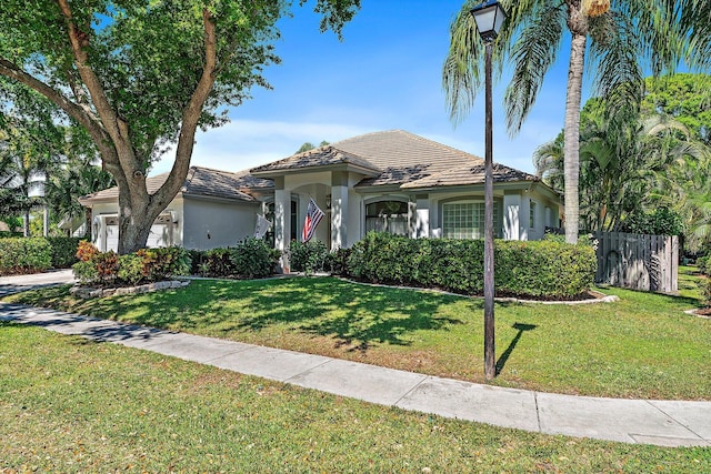 mediterranean / spanish house with a front lawn, fence, an attached garage, and stucco siding