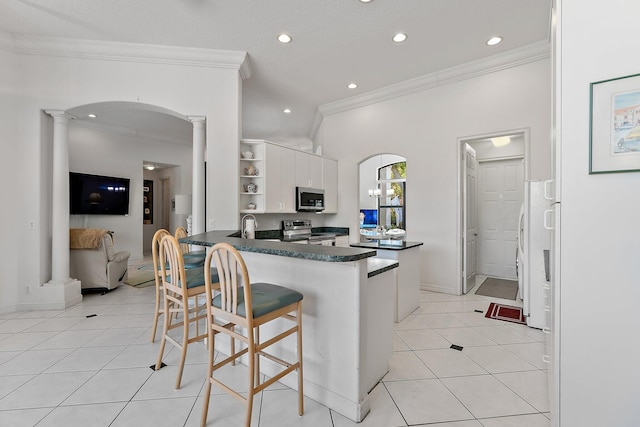 kitchen featuring arched walkways, stainless steel appliances, open shelves, dark countertops, and ornate columns