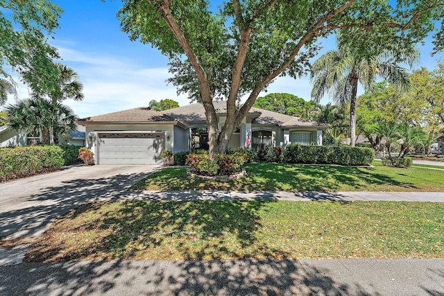 ranch-style house featuring a tile roof, stucco siding, a garage, driveway, and a front lawn