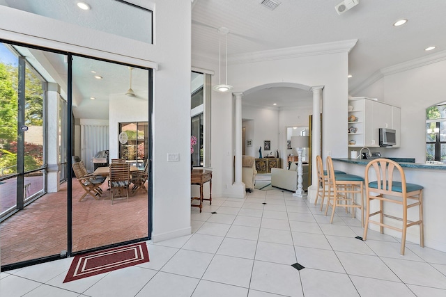 interior space with a healthy amount of sunlight, ornate columns, light tile patterned floors, and crown molding