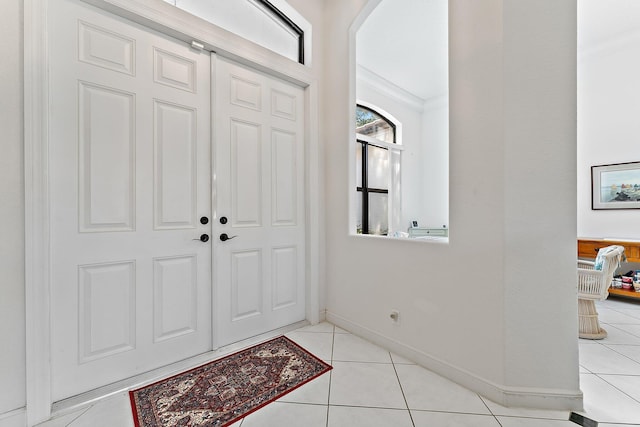 foyer entrance featuring arched walkways, light tile patterned flooring, baseboards, and crown molding