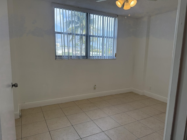 empty room featuring light tile patterned floors, baseboards, ceiling fan, and a textured ceiling