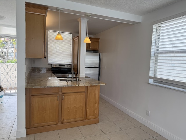kitchen featuring a peninsula, appliances with stainless steel finishes, light tile patterned flooring, a sink, and brown cabinets