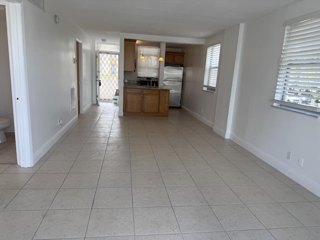 kitchen with light tile patterned floors, visible vents, baseboards, freestanding refrigerator, and brown cabinetry