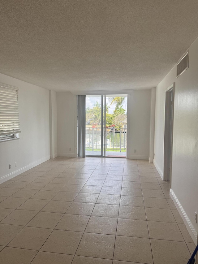 unfurnished room featuring visible vents, baseboards, light tile patterned floors, and a textured ceiling