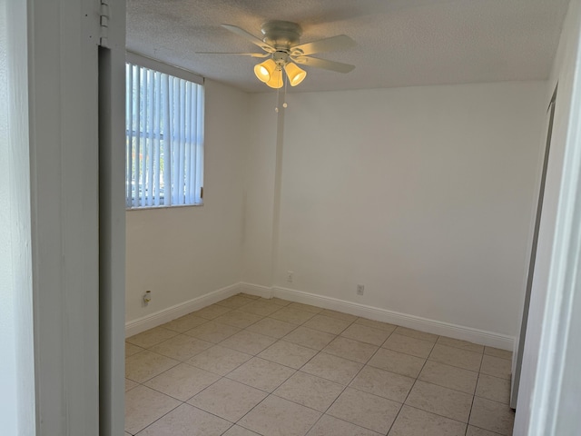 empty room with a textured ceiling, light tile patterned floors, baseboards, and a ceiling fan