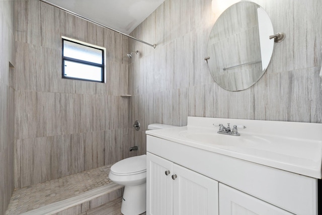 bathroom featuring tiled shower, tile walls, toilet, and vanity