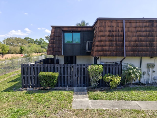 view of front facade with mansard roof, a fenced front yard, a front yard, and stucco siding