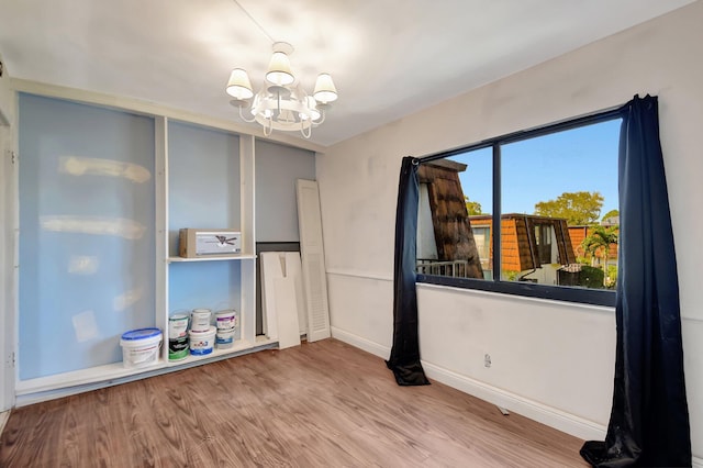 empty room featuring a chandelier, wood finished floors, and baseboards