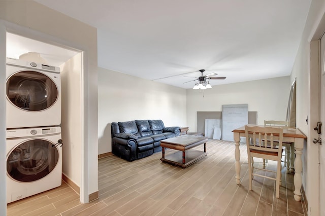 living room featuring a ceiling fan, wood finish floors, stacked washer and clothes dryer, and baseboards