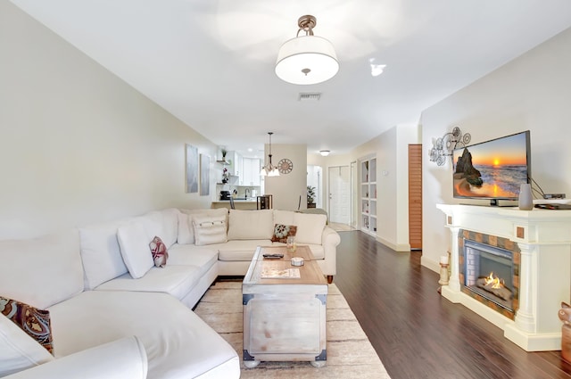 living area with visible vents, a glass covered fireplace, wood finished floors, a chandelier, and baseboards