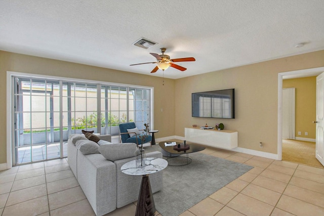 living room featuring light tile patterned floors, a textured ceiling, visible vents, baseboards, and a ceiling fan