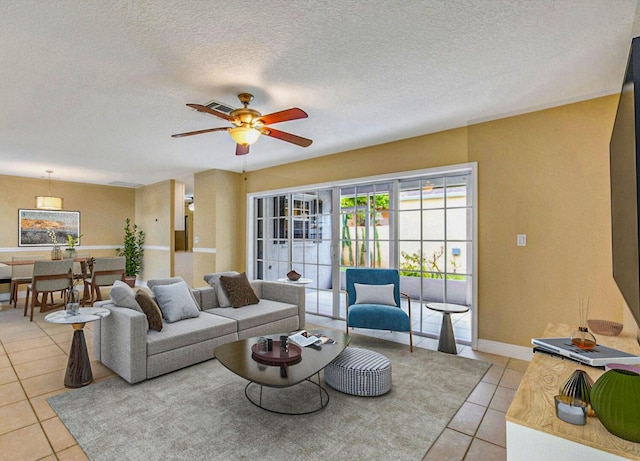 living room with light tile patterned floors, baseboards, a ceiling fan, and a textured ceiling