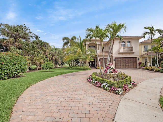 mediterranean / spanish house with decorative driveway, stucco siding, a front yard, a balcony, and a garage