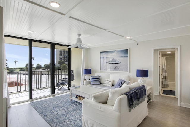 living area featuring expansive windows, wood finished floors, a ceiling fan, and baseboards