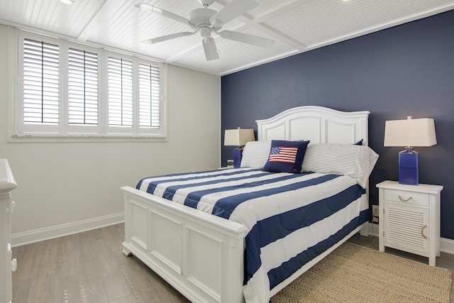 bedroom featuring a ceiling fan, beamed ceiling, light wood finished floors, and baseboards