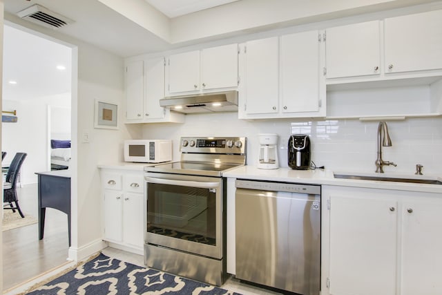 kitchen with visible vents, a sink, stainless steel appliances, under cabinet range hood, and backsplash