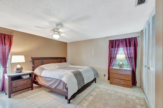 bedroom with visible vents, ceiling fan, a textured ceiling, a closet, and light tile patterned flooring