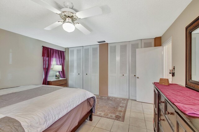 bedroom with ceiling fan, a textured ceiling, two closets, and light tile patterned flooring