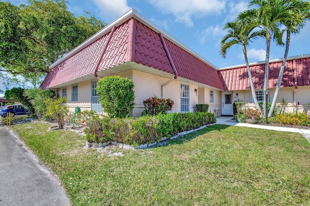 view of front of home with a tiled roof, a front yard, mansard roof, and stucco siding