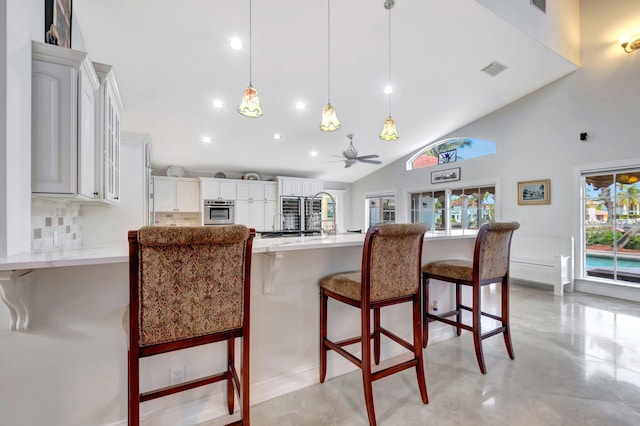 kitchen featuring a breakfast bar area, a peninsula, stainless steel oven, visible vents, and decorative light fixtures