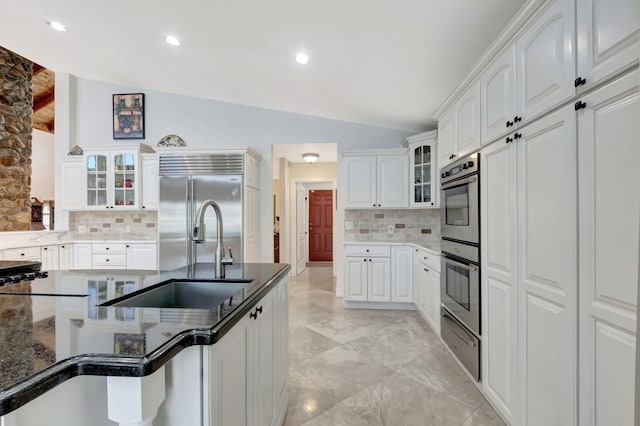 kitchen with dark stone counters, a sink, vaulted ceiling, appliances with stainless steel finishes, and a warming drawer