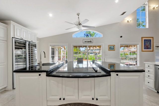 kitchen featuring an island with sink, lofted ceiling, refrigerator with glass door, white cabinetry, and a sink