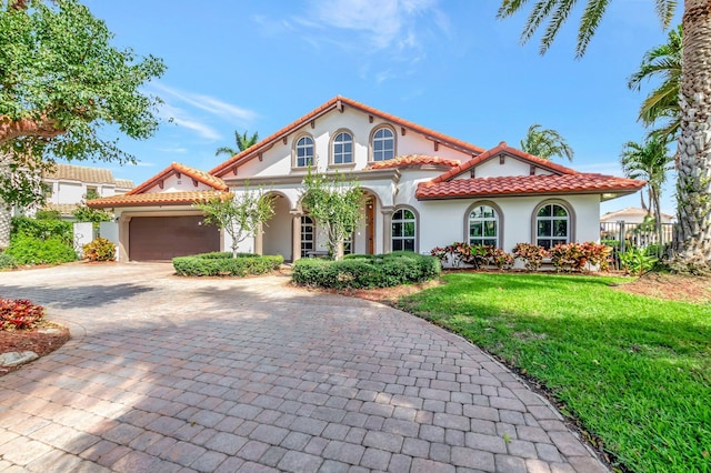 mediterranean / spanish house featuring decorative driveway, stucco siding, a garage, a tiled roof, and a front lawn