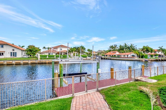 dock area featuring boat lift, a water view, a lawn, fence, and a residential view