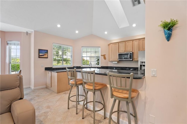 kitchen featuring stainless steel appliances, visible vents, light brown cabinetry, plenty of natural light, and a kitchen breakfast bar