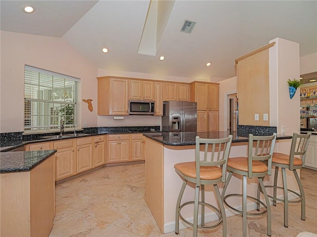 kitchen featuring visible vents, light brown cabinetry, appliances with stainless steel finishes, a sink, and dark stone countertops