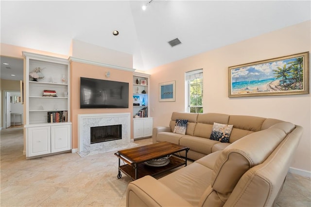 living area with high vaulted ceiling, built in shelves, a high end fireplace, visible vents, and baseboards