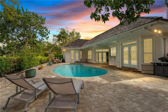 pool at dusk featuring french doors, a patio area, and an outdoor pool