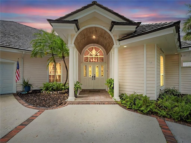 exterior entry at dusk with a garage, concrete driveway, and covered porch