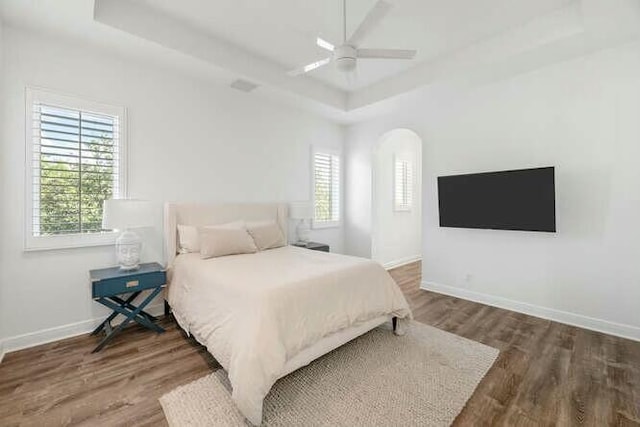 bedroom featuring arched walkways, baseboards, a raised ceiling, and wood finished floors