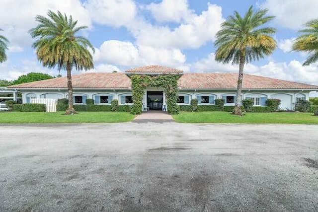 mediterranean / spanish house with a garage, driveway, a front lawn, and a tiled roof