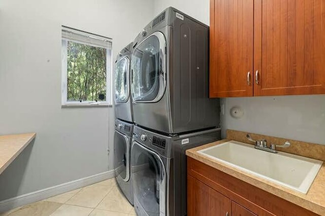 laundry area featuring light tile patterned flooring, stacked washer and dryer, a sink, baseboards, and cabinet space