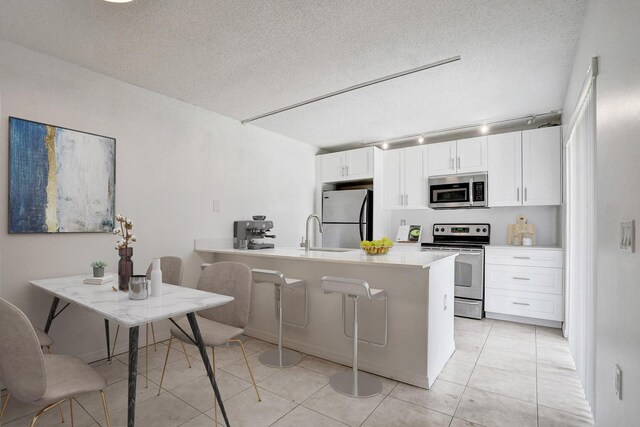 kitchen with a textured ceiling, appliances with stainless steel finishes, a sink, and white cabinets