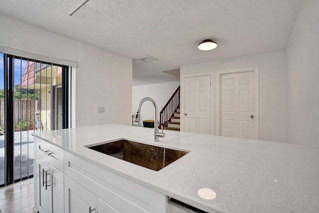 kitchen featuring light tile patterned floors, white cabinetry, a sink, a textured ceiling, and light stone countertops