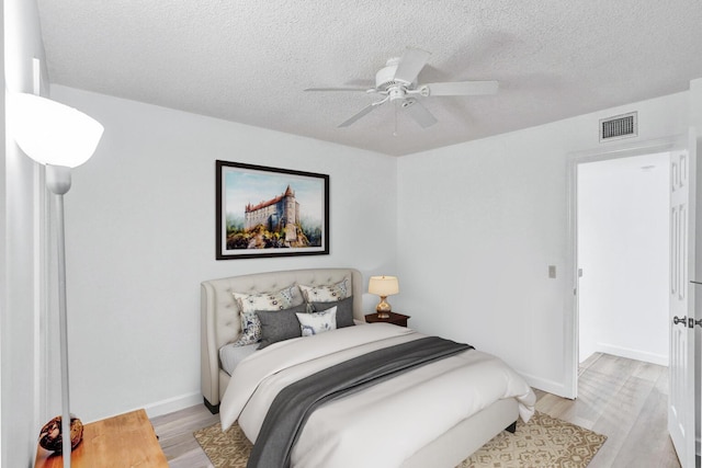 bedroom with visible vents, ceiling fan, a textured ceiling, light wood-type flooring, and baseboards