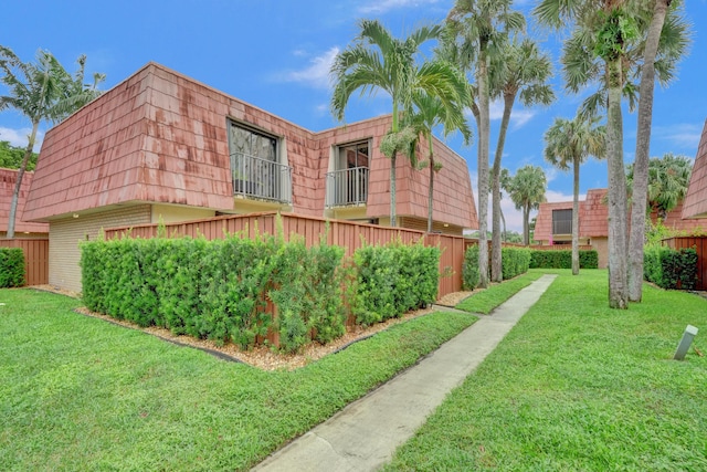 view of property exterior with brick siding, a lawn, fence, and mansard roof