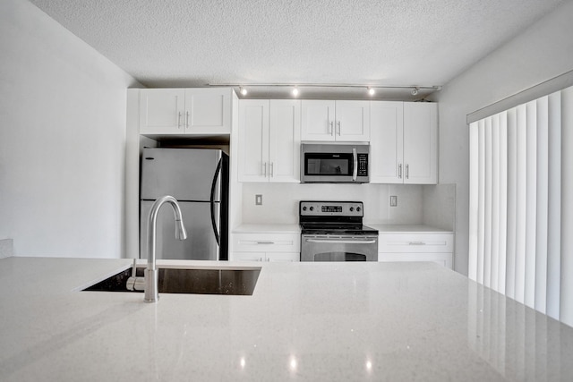 kitchen with a textured ceiling, appliances with stainless steel finishes, a sink, and white cabinetry