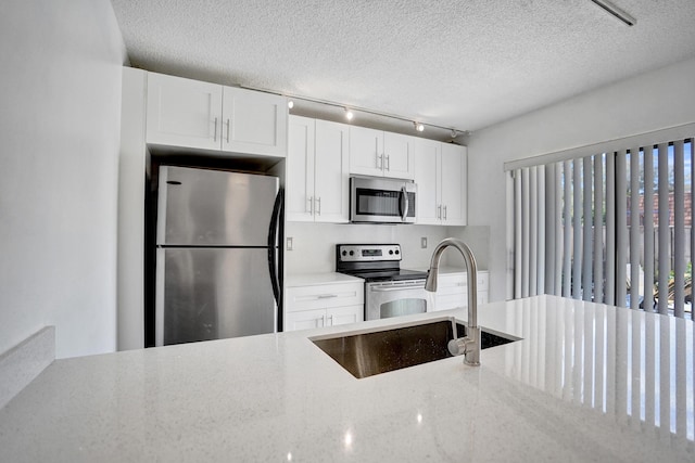 kitchen with white cabinets, appliances with stainless steel finishes, light stone counters, a textured ceiling, and a sink