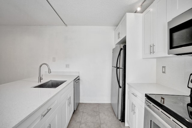 kitchen featuring light tile patterned floors, white cabinets, stainless steel appliances, a textured ceiling, and a sink