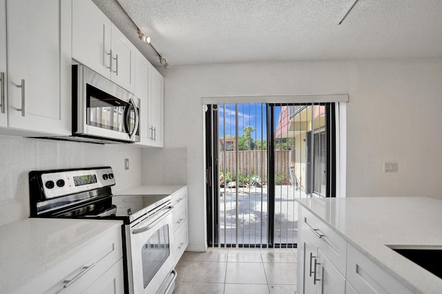 kitchen with a textured ceiling, light tile patterned flooring, white cabinets, appliances with stainless steel finishes, and rail lighting