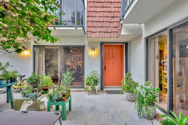 property entrance with a tiled roof, mansard roof, a balcony, and stucco siding